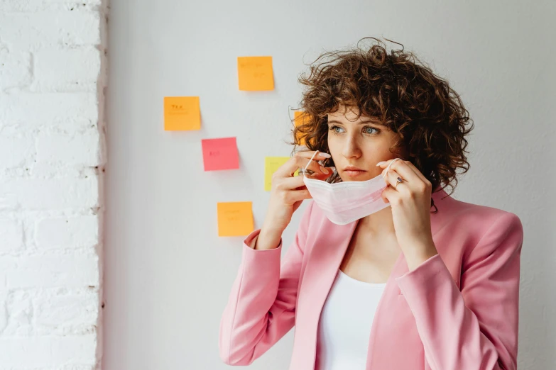 a woman standing in front of a wall covered in sticky notes, trending on pexels, happening, surgical mask covering mouth, white and pink cloth, avatar image, pondering