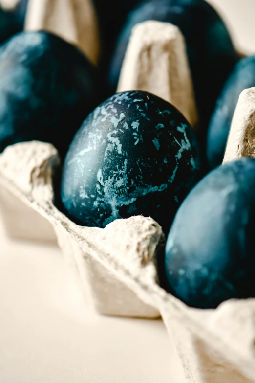 a carton filled with blue eggs sitting on top of a table, obsidian accents, black textured, thumbnail, up-close