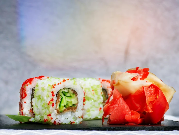 a piece of sushi sitting on top of a black plate, by Julia Pishtar, unsplash, mingei, vibrant red and green colours, blue and red, background image