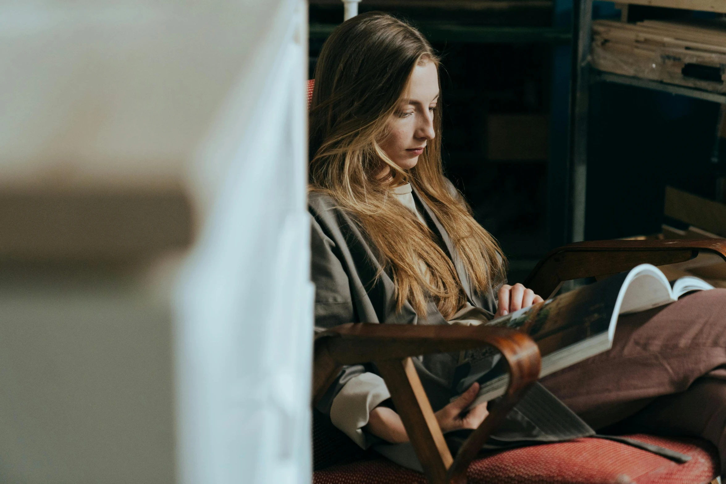 a woman sitting in a chair reading a book, by Emma Andijewska, pexels contest winner, girl with long hair, sitting in a waiting room, studious, serious focussed look