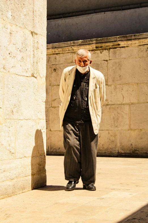 a man standing in front of a stone wall, by Peter Churcher, unsplash, baroque, old man doing with mask, jerusalem, wearing hakama, sunny summer day