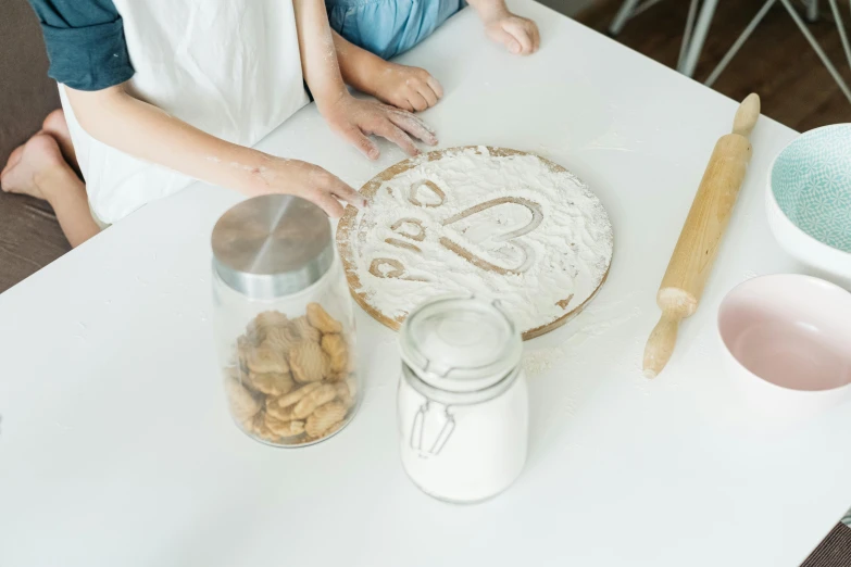 a couple of people that are sitting at a table, an album cover, by Nina Hamnett, trending on pexels, baking cookies, white, metal lid, with a kid