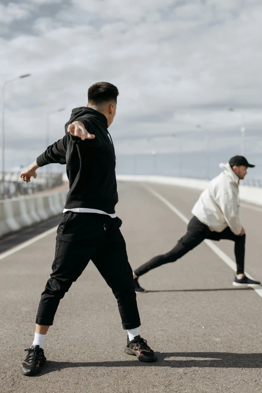 a couple of men standing on top of a road, dynamic stretching, wearing a hoodie and sweatpants, federation clothing, 2019 trending photo