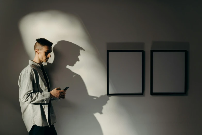 a man standing against a wall using a cell phone, a poster, by Adam Marczyński, trending on pexels, visual art, faces covered in shadows, in an art gallery], detective, gallery lighting