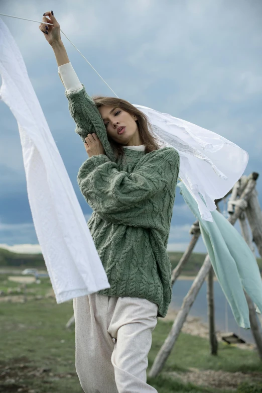 a woman standing next to a pile of clothes, inspired by Louisa Matthíasdóttir, trending on unsplash, renaissance, wearing a green sweater, windy day, off - white collection, model posing