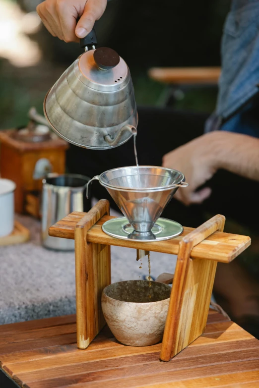 a person pouring a cup of coffee on top of a wooden table, tengri, outside, on display, straining