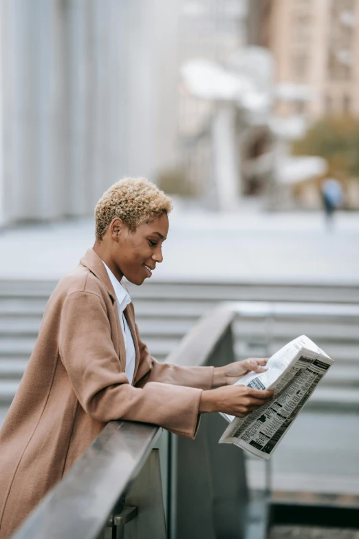 a woman sitting on a ledge reading a newspaper, by Cosmo Alexander, trending on unsplash, short blonde afro, wearing a worn out brown suit, androgynous male, holding a book