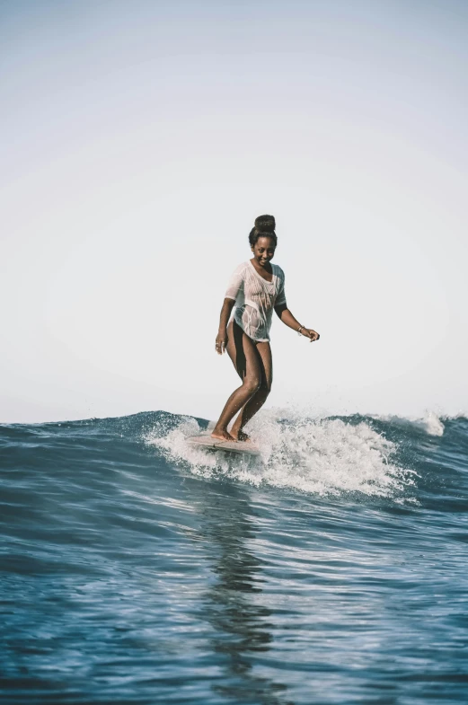 a woman riding a wave on top of a surfboard, tan skin a tee shirt and shorts, instagram picture, reggae, confidence