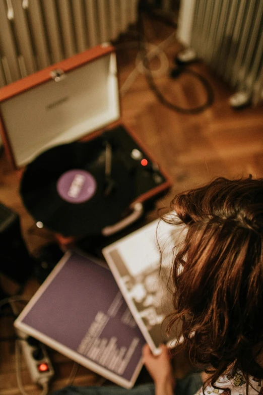 a woman sitting on top of a wooden floor next to a record player, inspired by Elsa Bleda, trending on pexels, private press, wearing purple headphones, facing away, sheet music, center of image