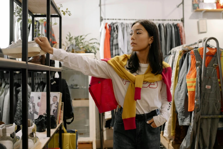 a woman standing in front of a rack of clothes, trending on pexels, happening, wearing shoulder cape, artist wearing overalls, wearing red and yellow clothes, a young asian woman