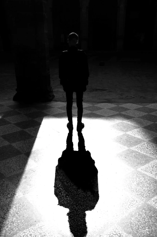 a black and white photo of a person standing in a dark room, a black and white photo, by Zsolt Bodoni, conceptual art, in a large cathedral, stand on stone floor, the sun shines in, faceless people