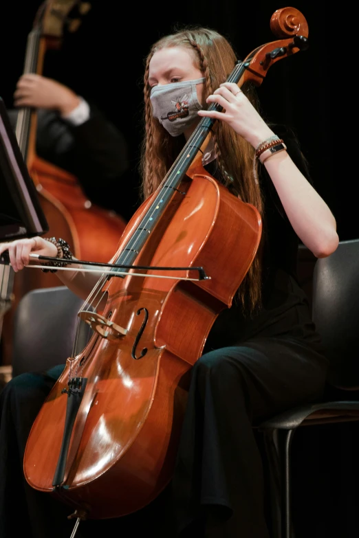 a woman in a mask playing a cello, high school, live concert photography, rectangle, featured