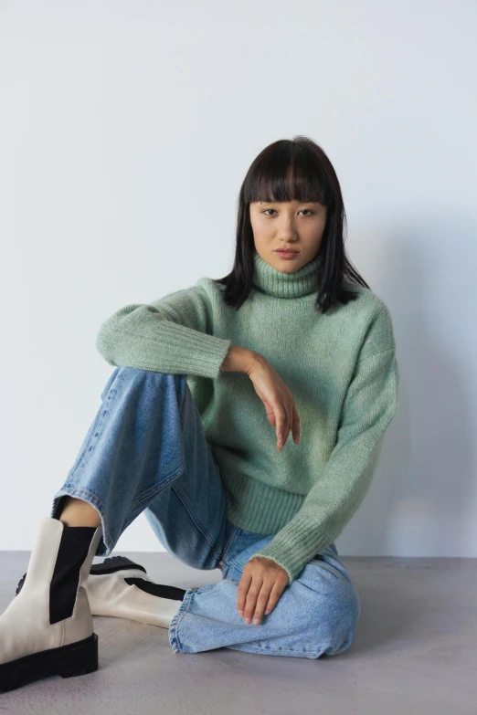 a woman sitting on the floor next to a pair of boots, inspired by Kim Tschang Yeul, gradient pastel green, wearing turtleneck, promotional image, wearing casual sweater