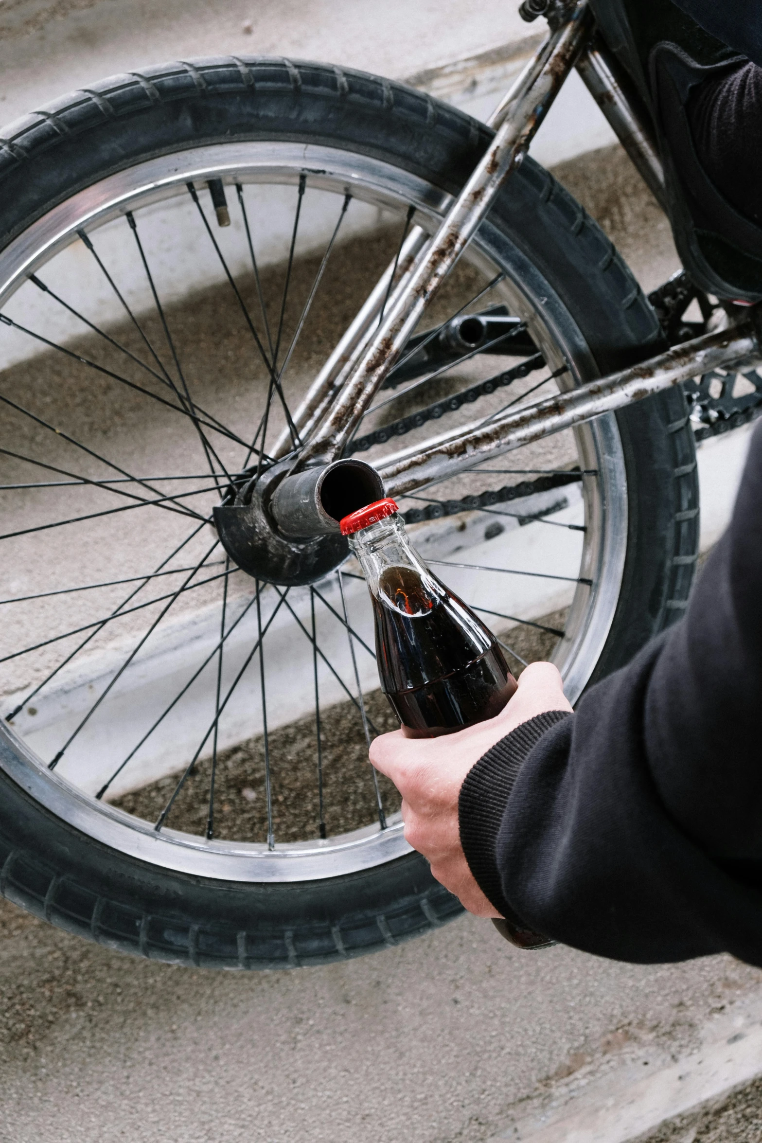 a person holding a bottle of beer next to a bicycle, slick tires, pouring, brown, no cropping