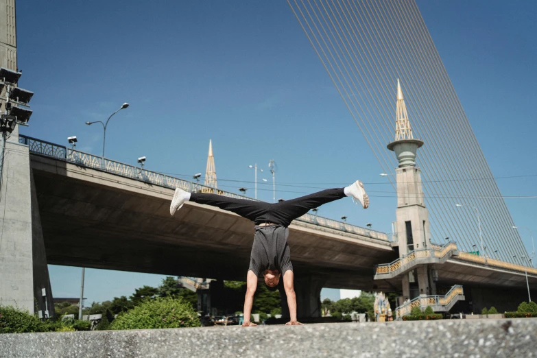 a man doing a handstand in front of a bridge, arabesque, nuri iyem, profile image, thumbnail, in the middle of the city