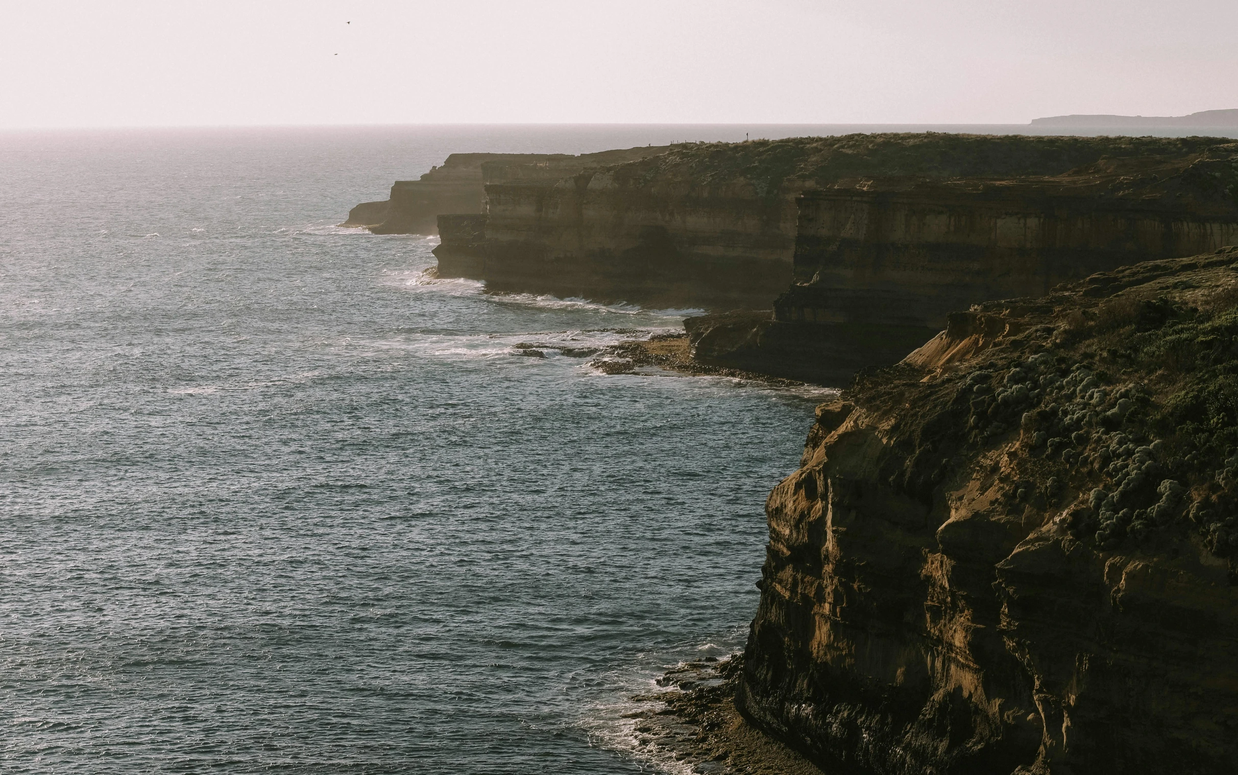 a man standing on top of a cliff next to the ocean, pexels contest winner, australian tonalism, coastal cliffs, sandstone, distant view, marsden