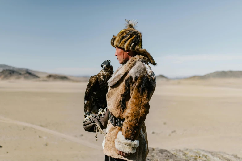 a man standing in the desert with a bird on his arm, a portrait, by Dietmar Damerau, pexels contest winner, wearing fur armor, avatar image, mongol, eagles