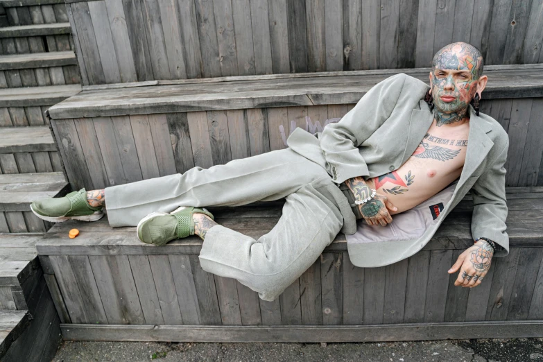 a man that is laying down on some steps, inspired by Seb McKinnon, trending on pexels, hyperrealism, fully tattooed body, grey suit, greenish skin, die antwoord style wear