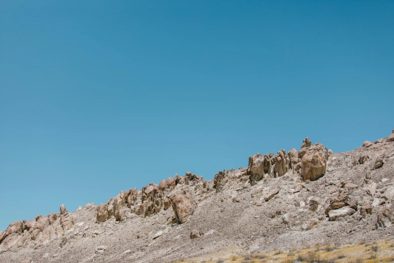 a man riding a motorcycle down a dirt road, an album cover, unsplash, figuration libre, extremely detailed rocky crag, clear blue sky, wes anderson background, seen from afar