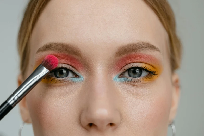 a close up of a person with a makeup brush, inspired by Louisa Matthíasdóttir, trending on pexels, yellow and red color scheme, pink and blue colour, easy to use, smokey eyes