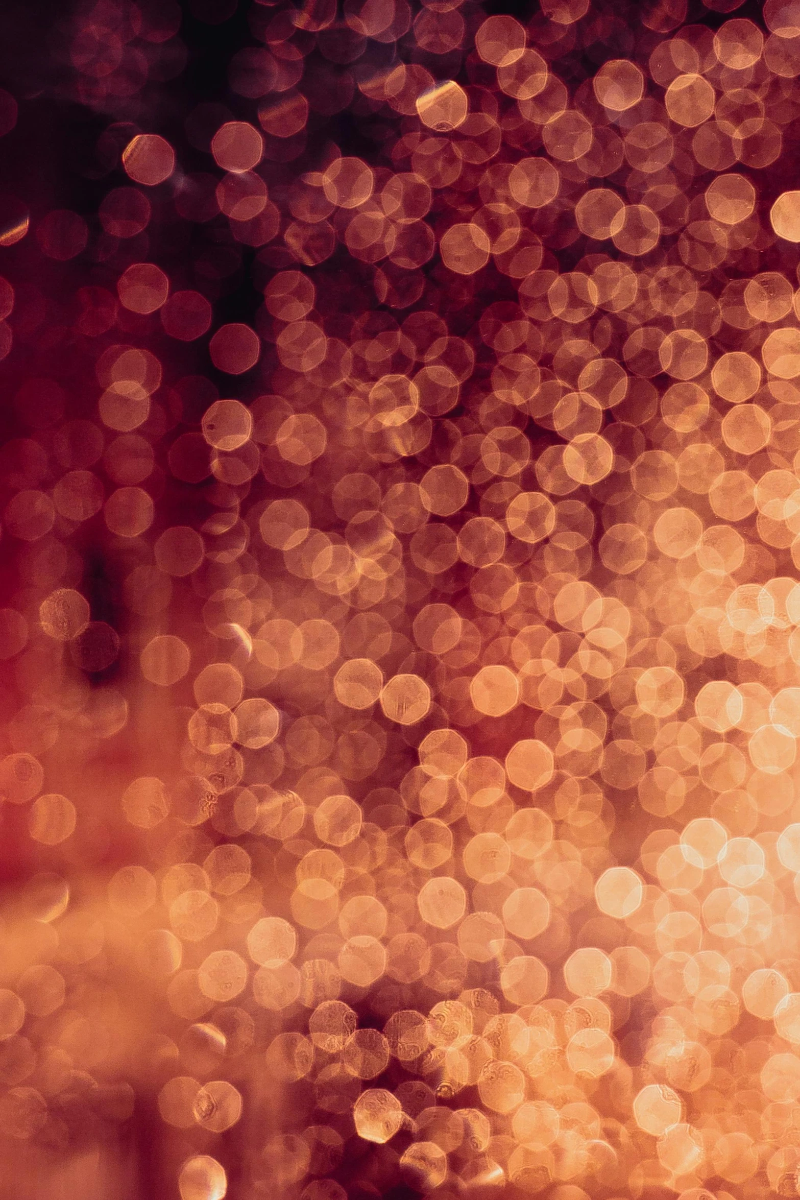 a wine glass sitting on top of a table, an album cover, inspired by Elsa Bleda, light and space, gold raining in the background, light red and deep orange mood, close - up bokeh, scattered light