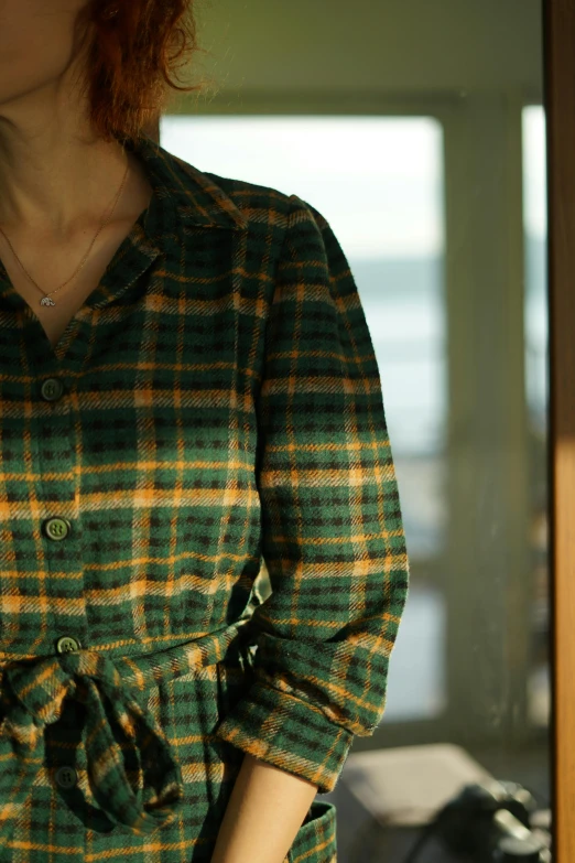 a woman standing in front of a mirror with her hands in her pockets, by Aguri Uchida, unsplash, tartan garment, gold and green, close up of lain iwakura, sundown