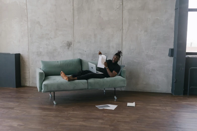 a man sitting on a couch reading a book, inspired by Michael Gustavius Payne, pexels contest winner, postminimalism, wangechi mutu, office furniture, green corduroy pants, in the middle of an empty room