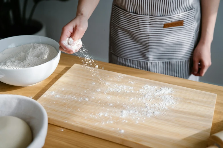 a person sprinkling flour onto a wooden cutting board, inspired by Yukimasa Ida, trending on unsplash, covered in salt, wearing an apron, detail shot, demo scene