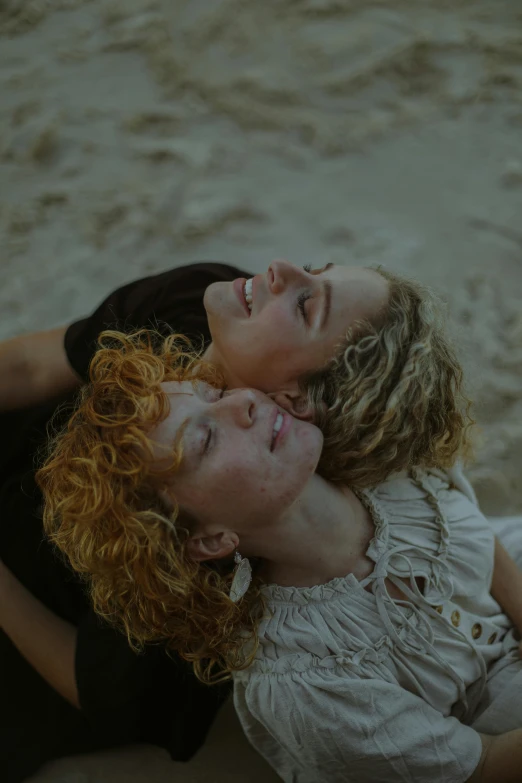 a couple of women laying on top of a sandy beach, inspired by Nan Goldin, trending on pexels, renaissance, short curly blonde haired girl, lesbian embrace, headshot, ignant