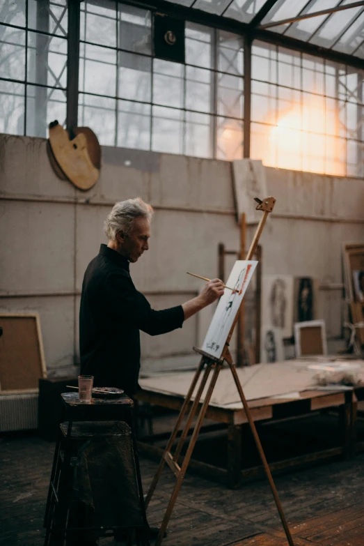 a man that is standing in front of a easel, holding a paintbrush