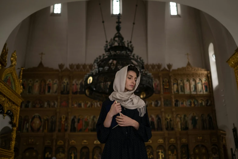 a woman in a black dress standing in a church, by Julia Pishtar, unsplash contest winner, qajar art, head scarf, an olive skinned, ( ( theatrical ) ), gray