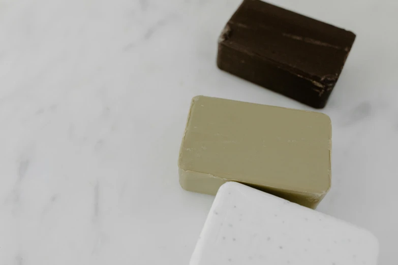a couple of soap bars sitting on top of a counter, inspired by Rachel Whiteread, unsplash, dark brown white green colours, fully chocolate, set against a white background, olive green