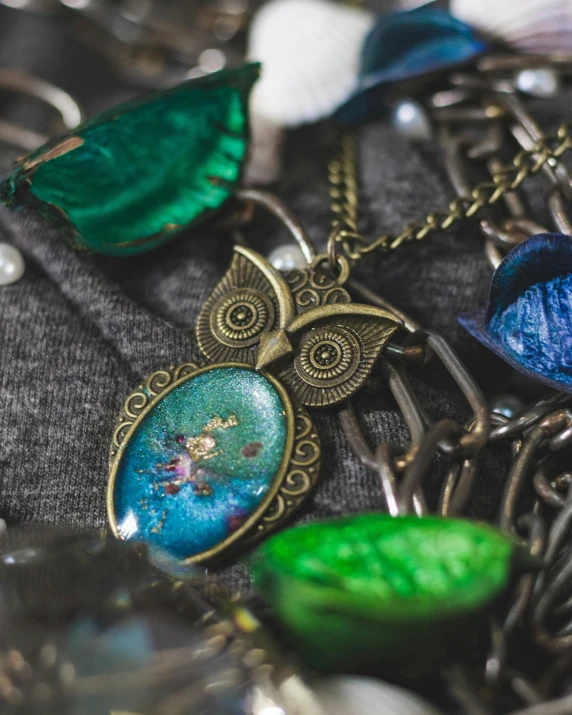 a pile of jewelry sitting on top of a table, inspired by Annie Rose Laing, pexels contest winner, process art, steampunk owl inside a glass jar, green and blue colour palette, high angle close up shot, wearing several pendants