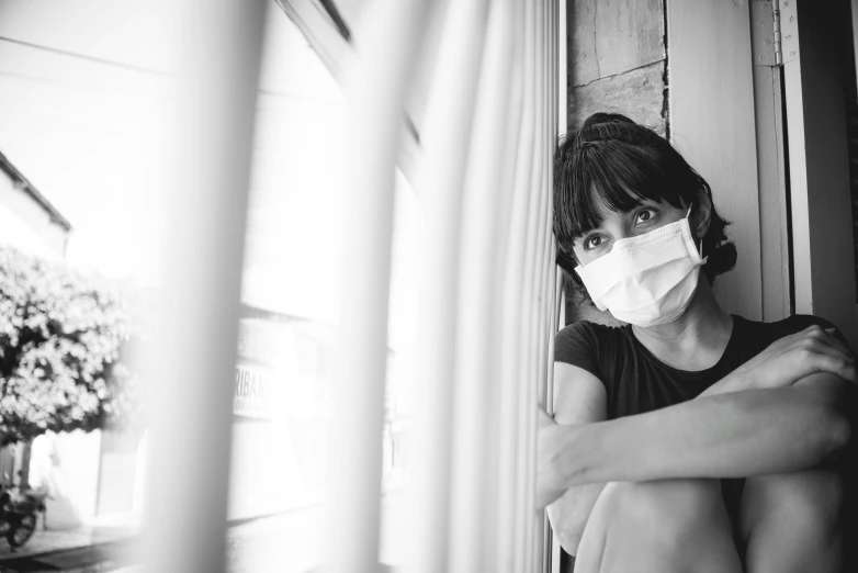 a black and white photo of a woman wearing a face mask, a black and white photo, pexels, sitting on a window sill, hiding behind obstacles, a young asian woman, healthcare worker