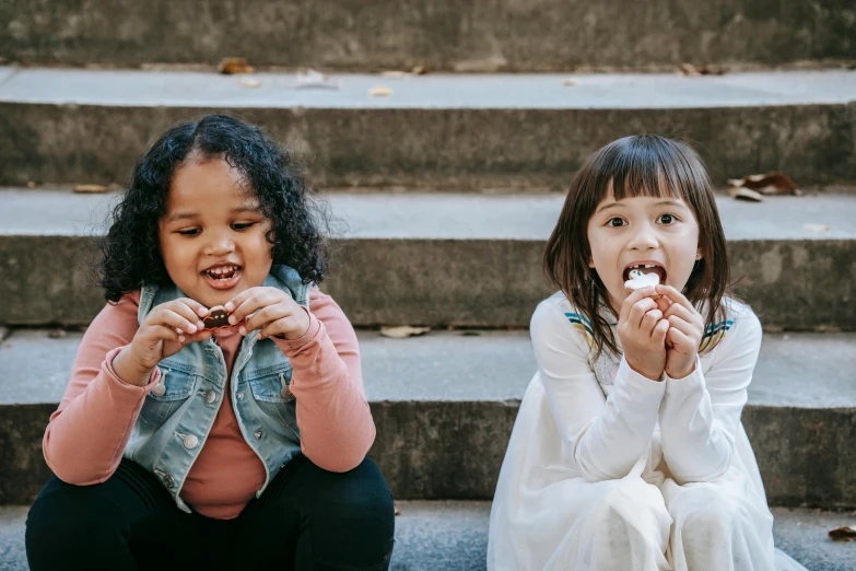 two little girls sitting on the steps eating donuts, by Emma Andijewska, pexels contest winner, teeth filled with cavities, mixed race, outside on the ground, chocolate