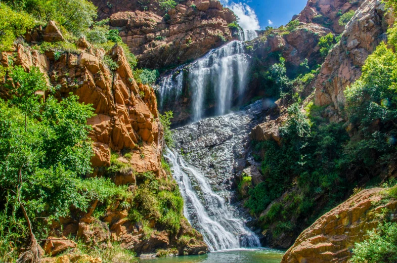 a waterfall in the middle of a canyon, by Hubert van Ravesteyn, unsplash, bushveld background, moroccan, “ iron bark, festivals