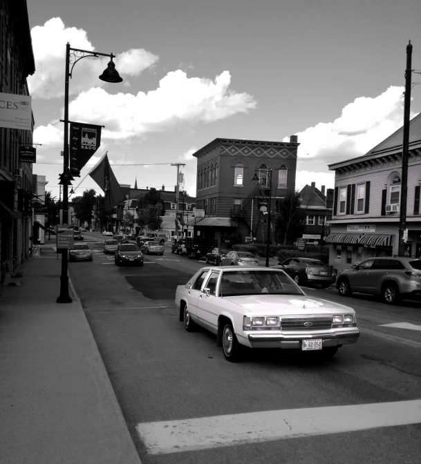 a white car driving down a street next to tall buildings, a black and white photo, busy small town street, chesley, bw photo, square