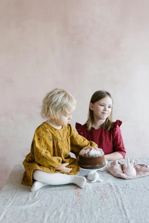 a couple of little girls sitting on top of a bed, inspired by Elsa Beskow, trending on unsplash, baking a cake, sitting on a mocha-colored table, studio lighting”, linen