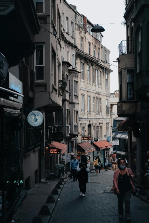 a group of people walking down a street next to tall buildings, istanbul, standing in an alleyway, background image, storefronts