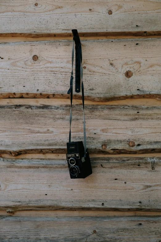a black camera hanging on a wooden wall, by Peter Churcher, leather straps, rustic wood, medium - shot, f/9
