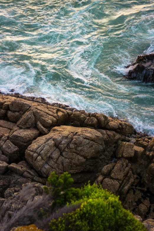 a man riding a surfboard on top of a rocky beach, an album cover, unsplash, ((rocks)), rivulets, wellington, high angle