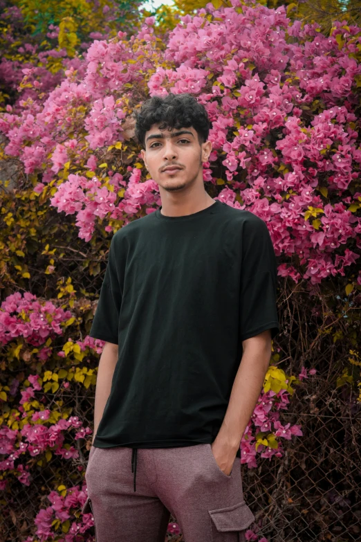 a young man standing in front of a bush of flowers, an album cover, inspired by John Luke, pexels contest winner, raden saleh, green shirt, wearing a black t-shirt, nonbinary model