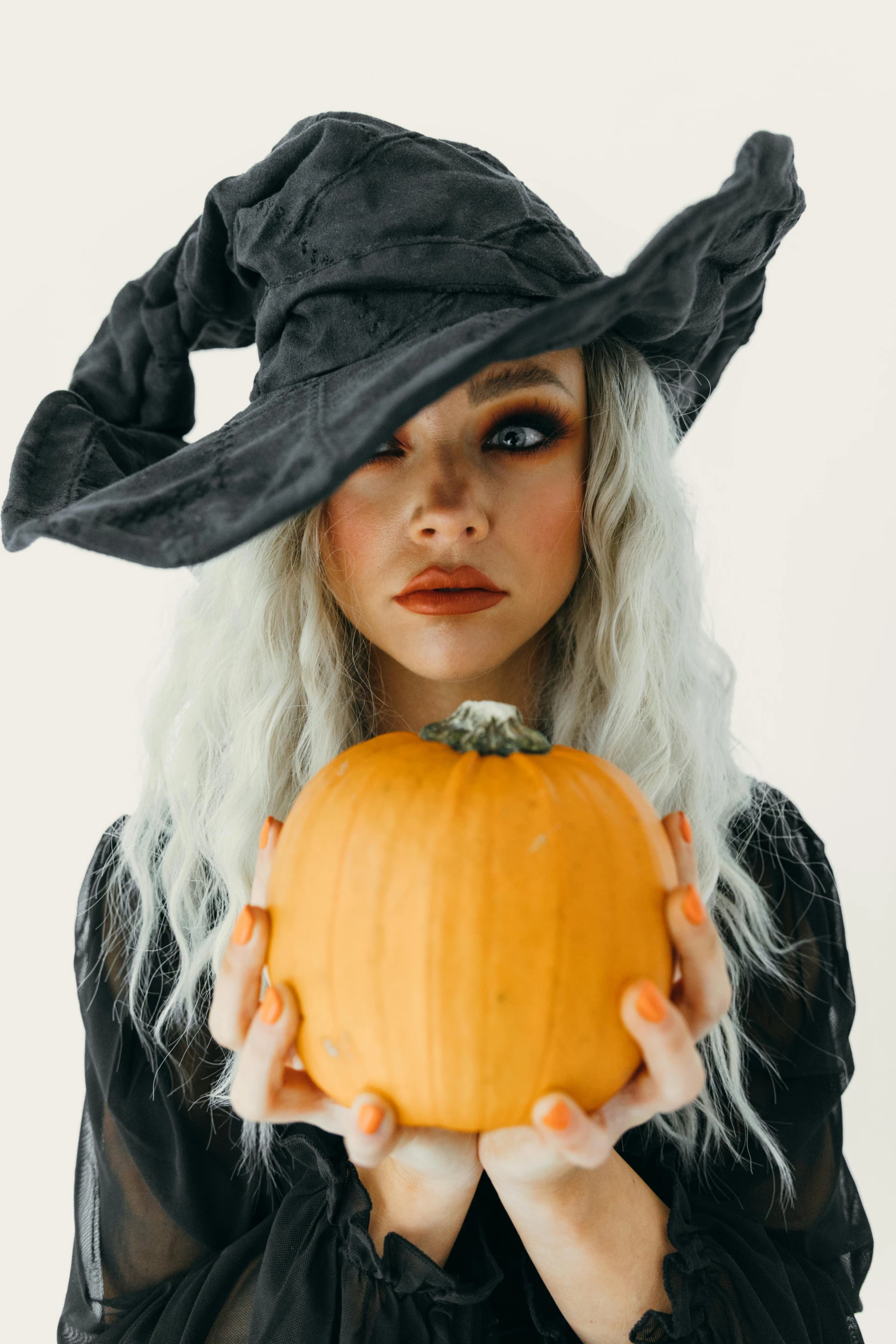 a woman in a witch hat holding a pumpkin, a colorized photo, trending on pexels, curled silver hair, square, gif, gen z