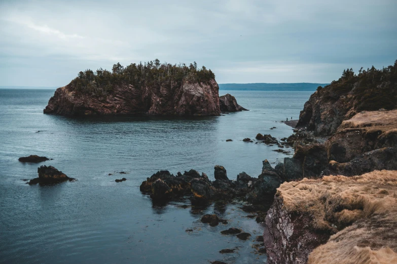 a small island in the middle of a body of water, pexels contest winner, coastal cliffs, dan ouellette, thumbnail, brown