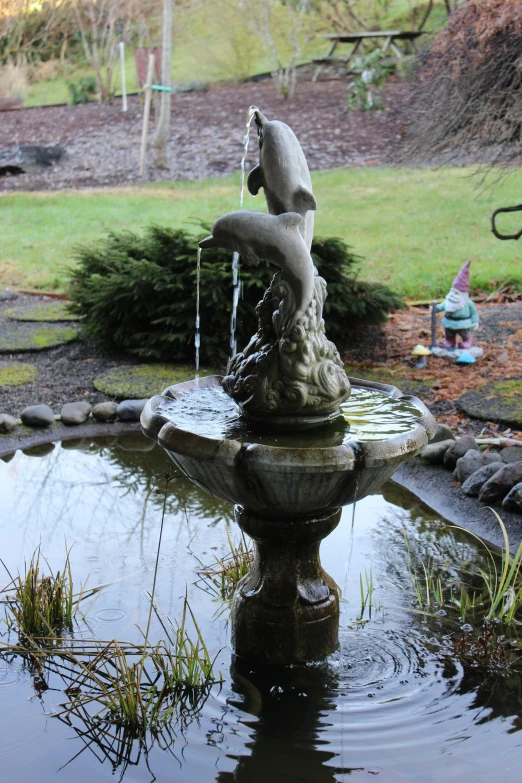 a bird that is sitting on top of a fountain, a statue, by Joe Sorren, back yard, swirling silver fish, wide shot!!!!!!, restored