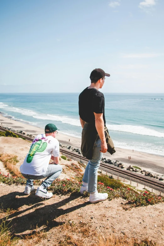 a couple of men standing on top of a hill next to the ocean, pexels contest winner, graffiti, outlive streetwear collection, southern california, train far, concert