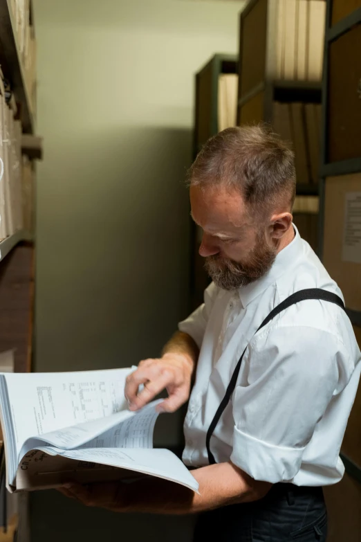 a man reading a book in a library, inspired by Peter Zumthor, white waist apron and undershirt, signing a bill, profile picture, in a kitchen