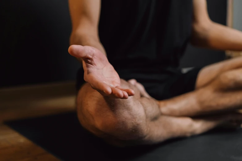 a man in a black shirt is sitting on a yoga mat, a picture, by Carey Morris, trending on pexels, the forefoot to make a v gesture, manuka, up to the elbow, from below
