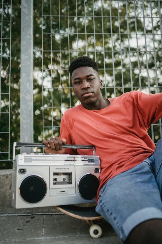 a man sitting on top of a skateboard next to a boombox, dark skinned, looking the camera, gen z, uploaded