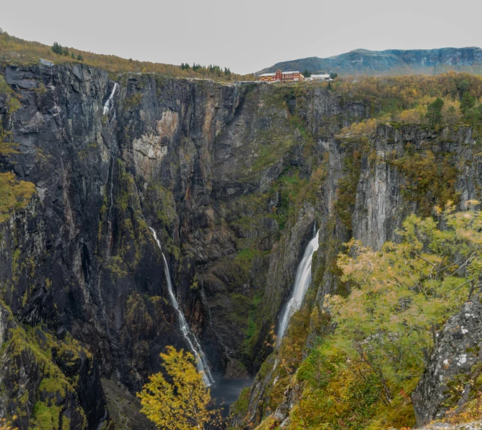 a man standing on top of a cliff next to a waterfall, by Roar Kjernstad, pexels contest winner, hurufiyya, panoramic view, mid fall, a beautiful mine, seen from a distance